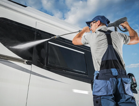 A man is diligently washing the window of a white RV, enhancing its cleanliness and visibility for travel.