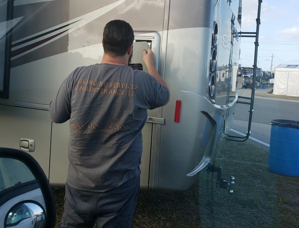 A man performs preventative maintenance by fixing the door of an RV, ensuring its proper function and safety.