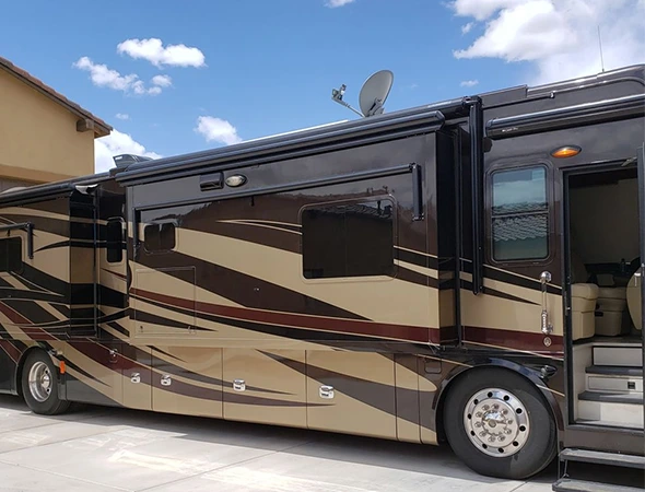 A spacious motor home is parked in a residential driveway, showcasing its size and design against the surrounding landscape.