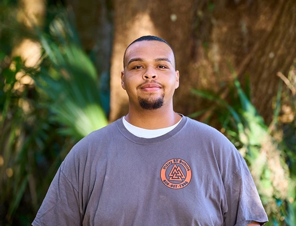 A man in a gray shirt stands confidently before a backdrop of trees, representing Viking RV Services' commitment to nature.