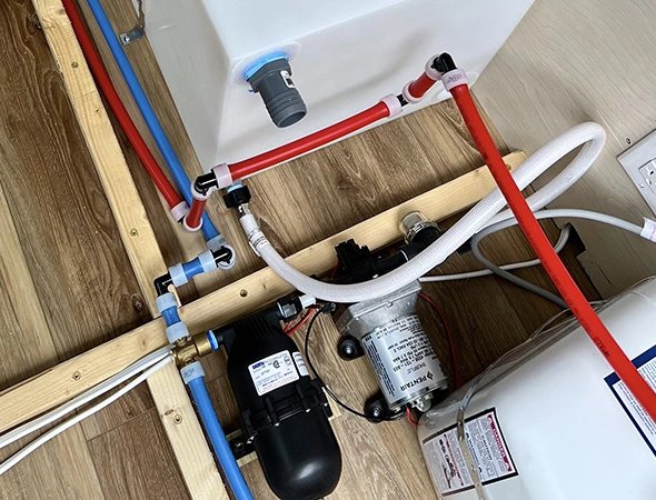 A water heater and pump are positioned on a wooden floor, showcasing essential plumbing equipment in a home setting.
