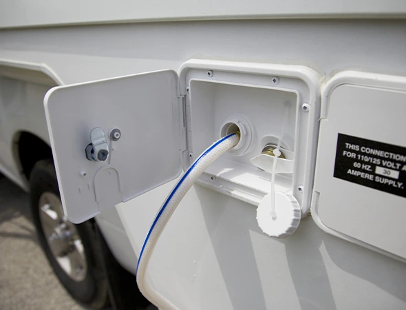 A white RV with a hose connected, indicating maintenance for a water tank replacement process.