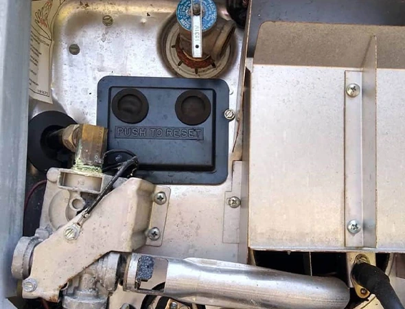 Close-up of a mechanical device with metal components, wiring, and a prominent black reset button labeled "PUSH TO RESET." The image conveys a technical and industrial feel.