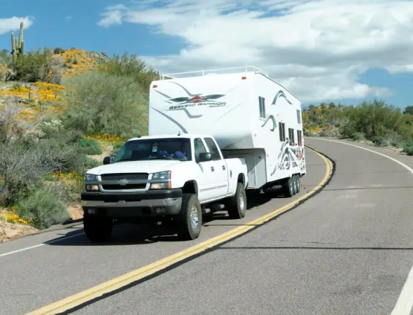 A white truck pulls an RV along a road, illustrating effective trailer and towing services for travel enthusiasts.